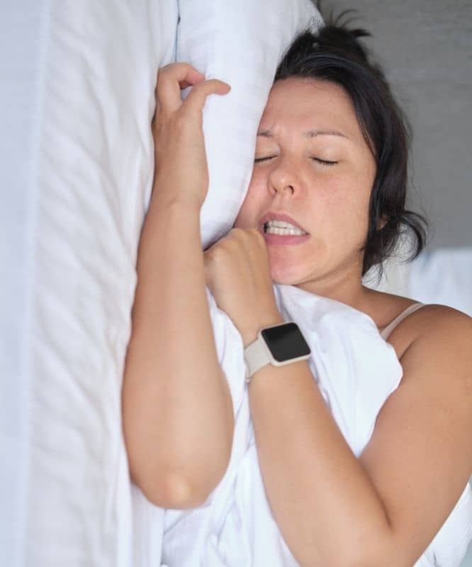 Woman clenching her teeth during sleep, illustrating sleep-related bruxism and nighttime jaw tension.