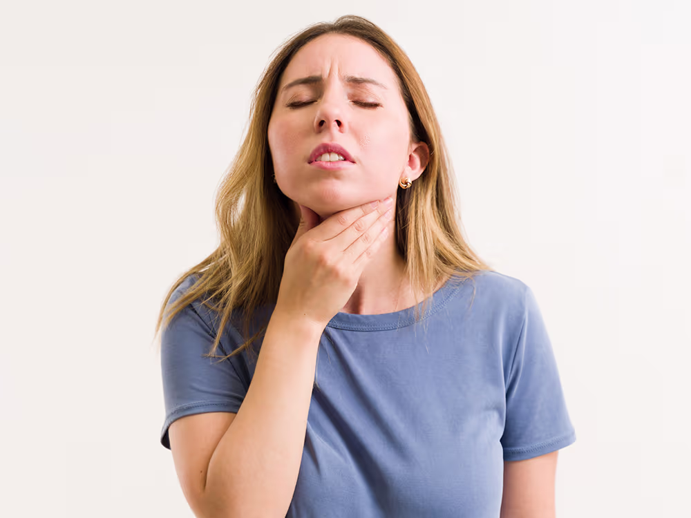 Woman holding her throat, illustrating common causes of laryngitis such as viral infections, reflux, and voice strain.