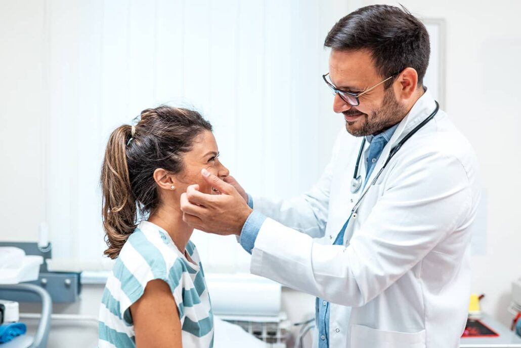 ENT specialist examining a patient during a consultation to review symptoms, perform an exam, and discuss treatment options.