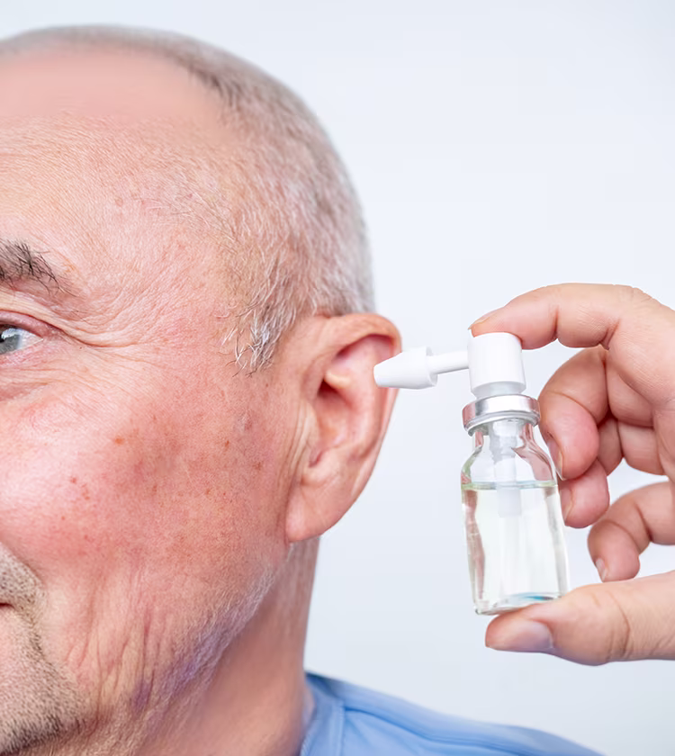 Adult using ear drops to help prevent ear wax buildup and maintain ear hygiene.