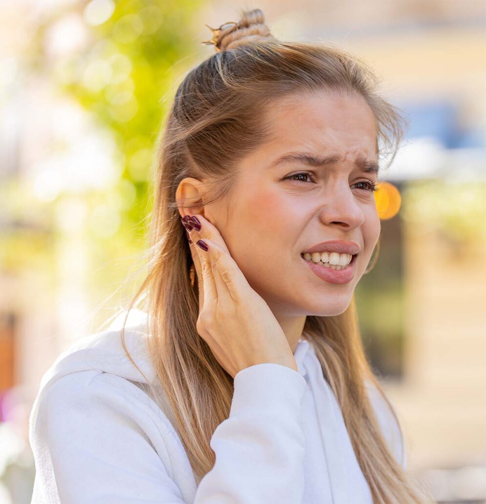Woman holding her ear in pain, illustrating sudden ear pain, dizziness, and hearing-related symptoms outdoors.
