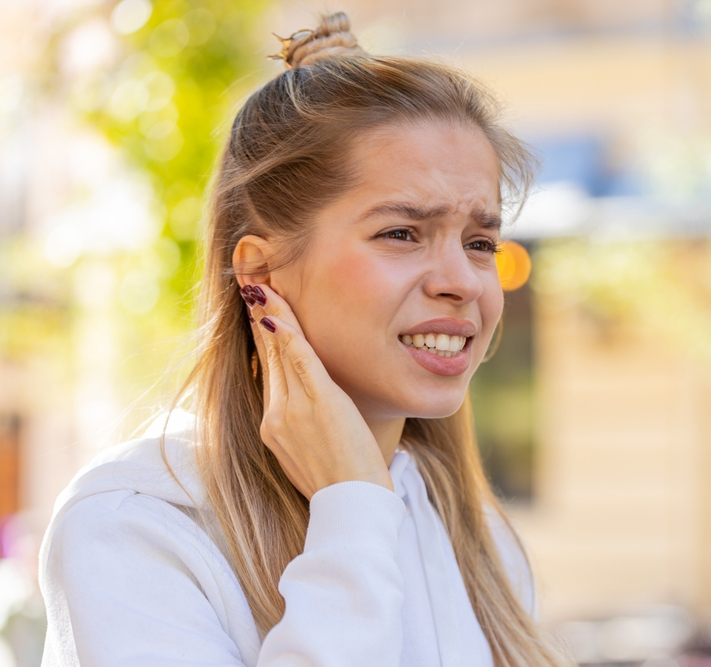 Woman holding her ear in pain, illustrating sudden ear pain, dizziness, and hearing-related symptoms outdoors.