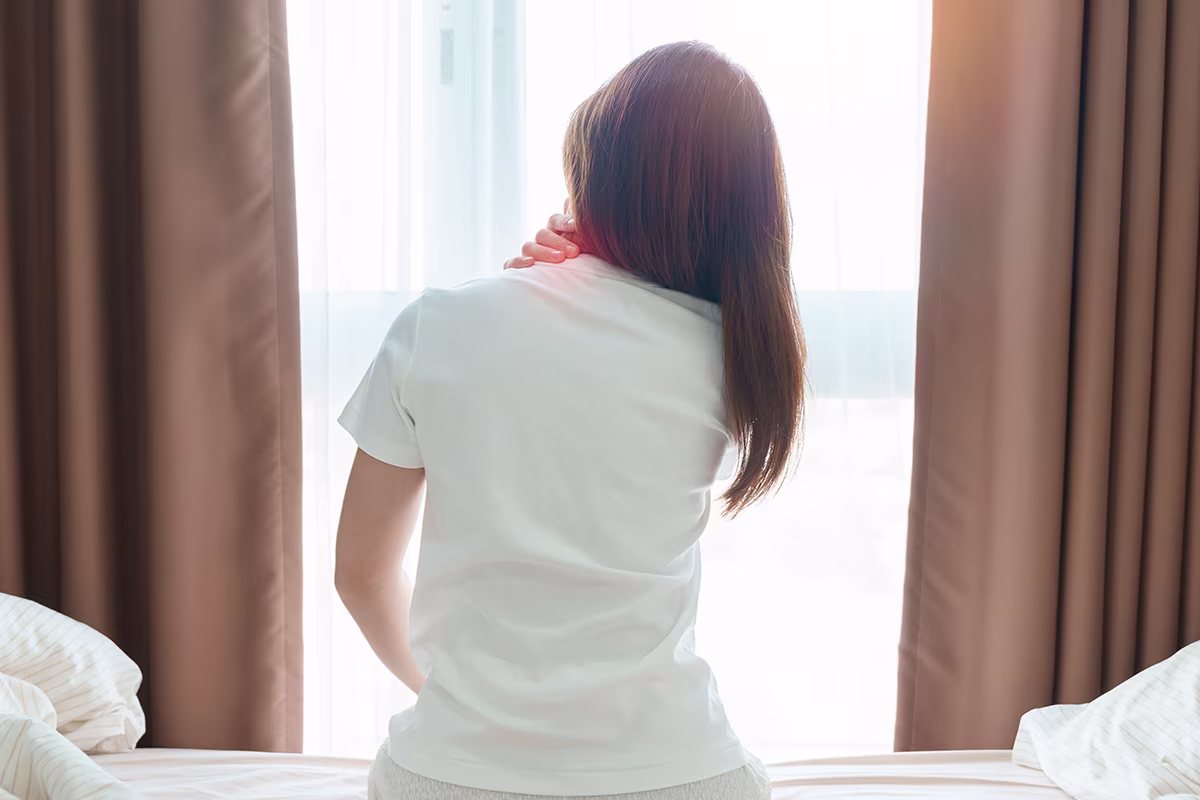 Person holding neck near window, representing head and neck cancer symptoms, pain, and related treatment concerns.