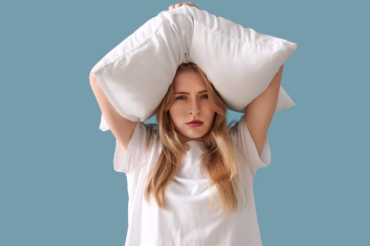 Woman holding a pillow over her head, representing insomnia symptoms and how sleep specialists evaluate disrupted sleep.