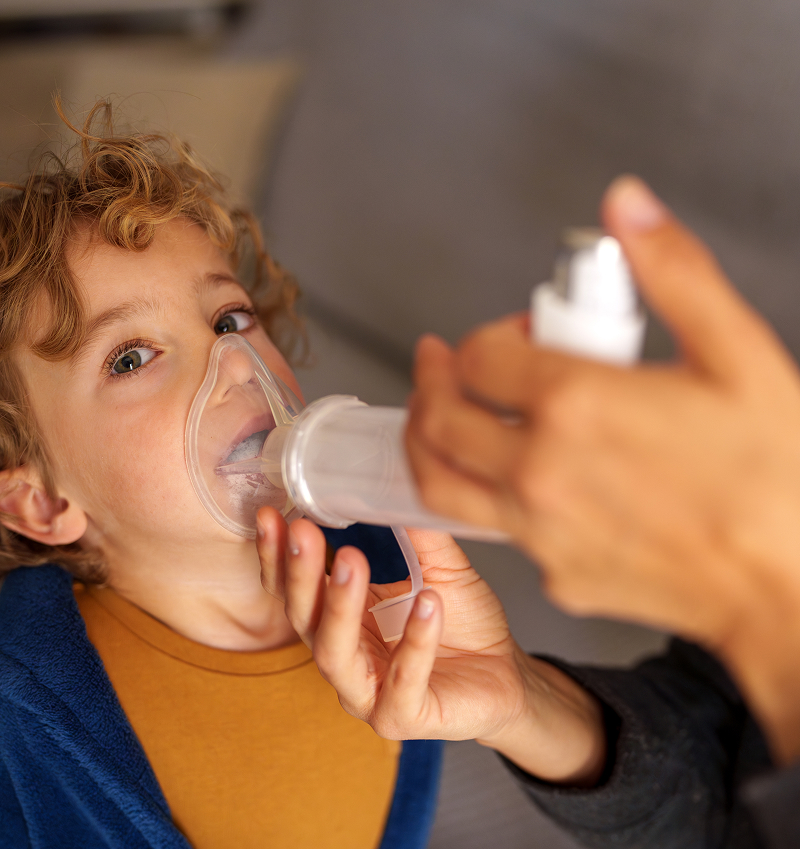 Young child using a nebulizer mask for asthma treatment while learning about pediatric asthma risks and breathing symptoms.