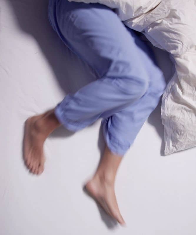 Person experiencing restless sleep and leg discomfort associated with Restless Legs Syndrome at night.