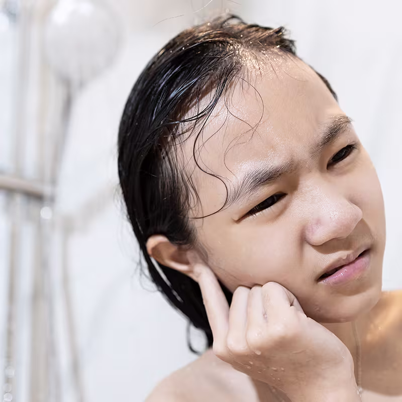 Person touching a painful ear after swimming, illustrating swimmer’s ear infection symptoms and discomfort.