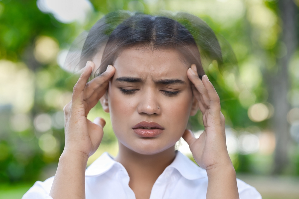 Woman experiencing vertigo and dizziness symptoms while holding her head outdoors with blurred motion effect.